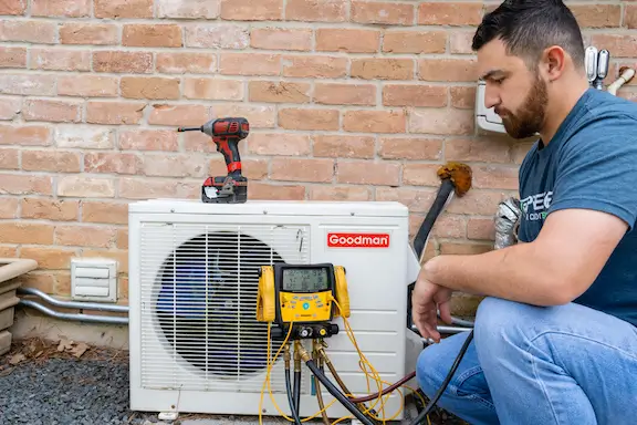 Prestige technician with manifold gauges connected to a Goodman outdoor condenser
